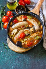 Stew smoked sausages with of beans, vegetables and tomato sauce in the pan on a stone countertop. Copy space.