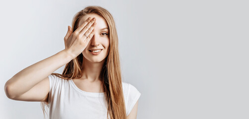 Young beautiful girl smiling and covering half of her face with hand on gray isolated background