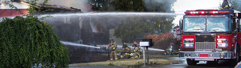 A residential home burns in a house fire as firefighters spay water from a hose in an effort to put it out. 