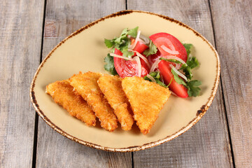 Georgian cuisine. Fried suluguni with tomato, onion and coriander salad in a beige plate on a wooden background. Rustic. Background image. Restaurant menu