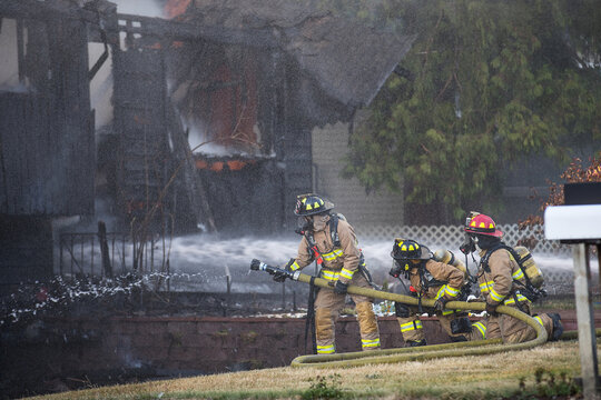 A residential home burns in a house fire as firefighters spay water from a hose in an effort to put it out. 