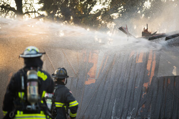 A residential home burns in a house fire as firefighters spay water from a hose in an effort to put it out. 