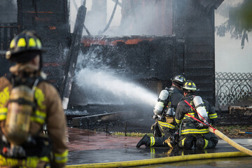 A residential home burns in a house fire as firefighters spay water from a hose in an effort to put...