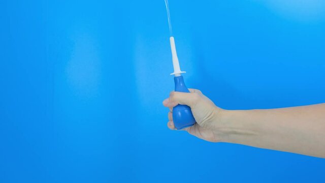 Hand with a blue enema puming, compressing, squeezing and injecting water on a blue background
