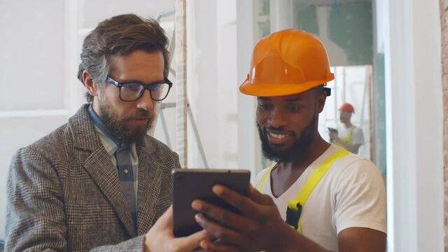 Portrait of caucasian architect and african builder discussing house blueprint on digital tablet