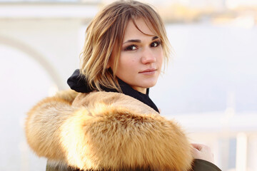  blond business woman in fox fir dawn jacket with hood closeup photo on city park background