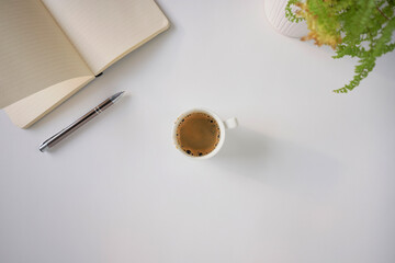 Top view of coffee cup and notebook on a white desk