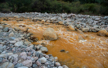 Yellow river called River of Gold due to the presence of iron in the water, flowing across the rocky valley, forest and mountains in La Rioja, Argentina.