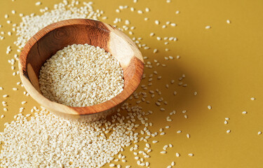 Tiny white sesame seeds in small wooden bowl, on yellow board, closeup photo