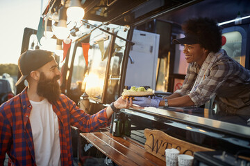 afro-american female employee gives with care sandwich to young hipster male customer