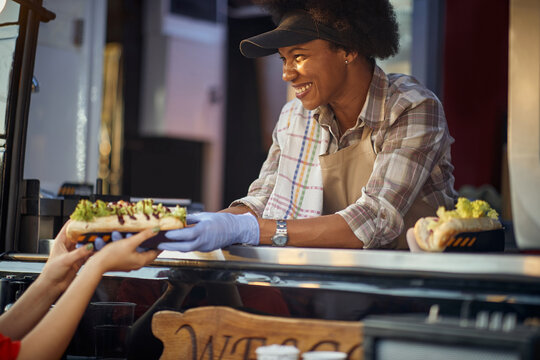 young afro-american female employee in fast food service giving ordered sandwiches to a customer with a smile