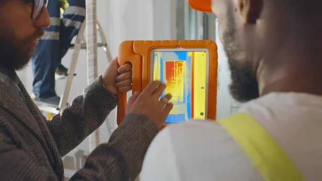 Back view of professional construction team using infrared camera on tablet checking heating system