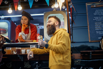 young  hipster eating sandwich in front of fast food service, socializing with female employee