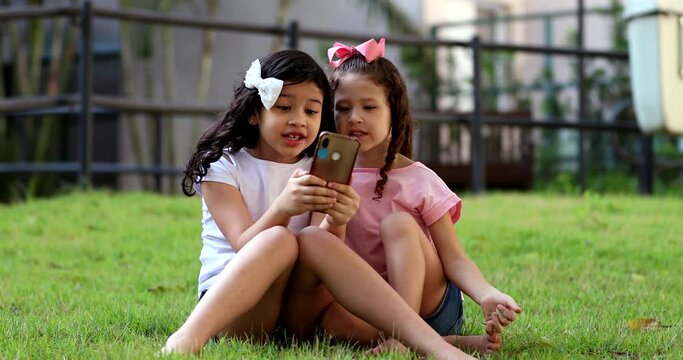 Children addicted to cellphone, two little girls looking at smartphone device on social media