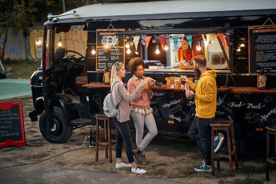 group of people socializing while eating outdoor in front of modified truck for fast food
