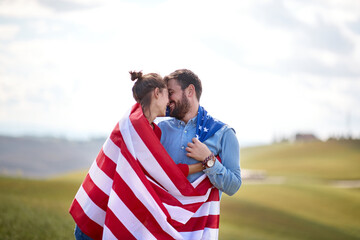 A couple in moments of love cloaked by American flag at a meadow. Election, campaign, freedom concept