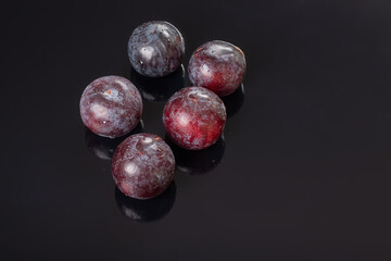 Five fresh plums on a black reflective background with water drops