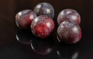 Five fresh plums on a black reflective background with water drops