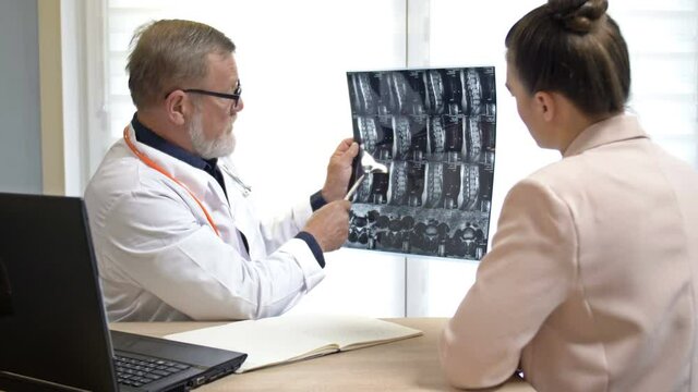 An experienced male doctor shows an X-ray image and explains the diagnosis to a young female patient during a consultation at a medical center.
