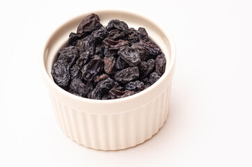 Black raisins in a light dish on a white background