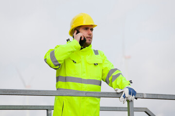 Young engineer or worker talking on smart phone in front of wind turbines