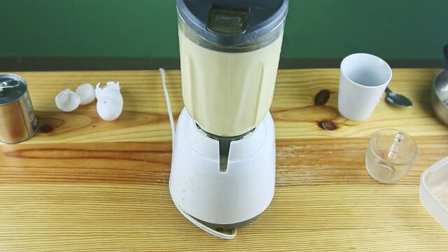 zoom out from electric blender mixing milk, condensed milk, and eggs