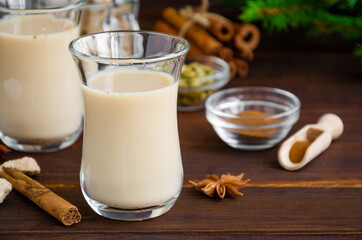 Hot tea with milk, cinnamon, cardamom, anise and other spices, Indian masala tea in a glass cup on a wooden background. Horizontal, copy space.