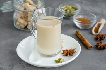 Obraz na płótnie Canvas Hot tea with milk, cinnamon, cardamom, anise and other spices, Indian masala tea in a glass on a dark background. copy space.