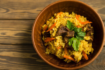 Rice with meat and herbs in a plate, on a wooden background. View from above