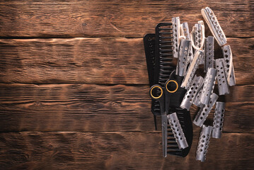 Old hair curlers, combs and scissors on the wooden table background.