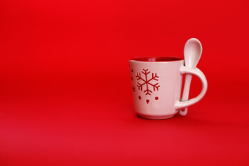 White mug with a spoon on a bright red background with a snowflake. Place for text, new year card, Christmas 2021 concept