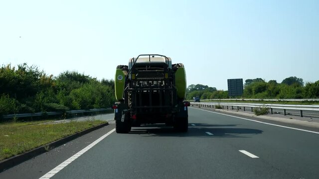 View from car following large farm vehicle driving slowly on motorway in England.
