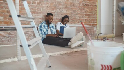 Young african couple during home renovation using laptop sitting on floor