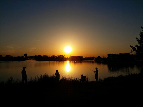 Three Men Fishing in the Lake Underneath the Sunset