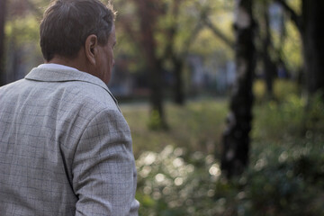 Senior man walking, hands clasped. Senior man walking and relaxing in park. Walking away, relaxing, rear view