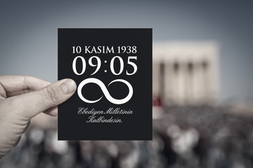 Hand holding a black paper with hour of the death and date of Ataturk in front of blurry Anitkabir...