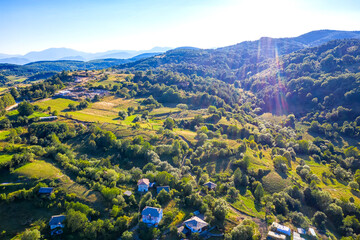 Aerial view from drone of beautiful mountain hills with houses and trees. Photo with sun flares