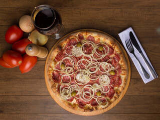 Pepperoni pizza with slices of onions, mozzarella cheese and green olives. Glass of wine, onions and rustic tomatoes to compose the photo. Top gastronomic photography.