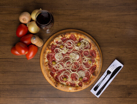 Pepperoni pizza with slices of onions, mozzarella cheese and green olives. Glass of wine, onions and rustic tomatoes. Top gastronomic photography with edges for texts.