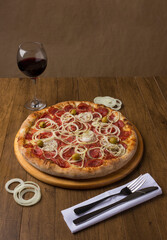 Pepperoni sausage pizza with sliced ​​onions and green olives. Glass of Red Wine to accompany the meal. Brazillian tipical food. Similar to Pepperonie's pizza. Vertical photo.