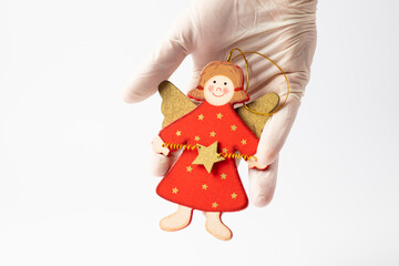 Wooden Christmas angel held in a hand in a protective glove on a white background. Christmas concept during a pandemic.