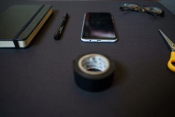 Work area on a black table, smartphone, scissors, pen, book, notebook, glasses