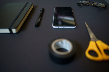 Work area on a black table, smartphone, scissors, pen, book, notebook, glasses