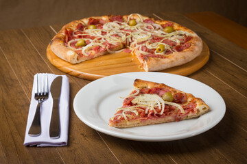 Tasty slice of pepperoni pizza made with slices of onions, mozzarella cheese and green olives. Pizza on the plate. Gastronomic food photography.
