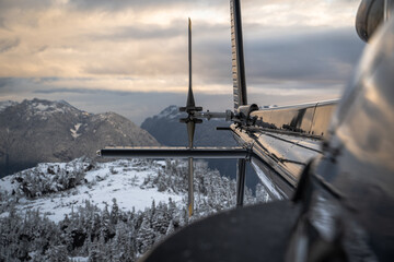 Looking Down the Side of a Black Helicopter Towards the Tail Rotor Over Snowy Mountains