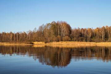 The autumn forest is reflected in the water surface of the lake. The concept of a quiet, private holiday during the coronavirus pandemic. Horizontal orientation