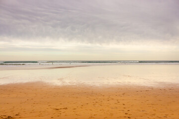 Wide panoramic beach with dramatic sky, bay of Biscay. Surf concept. Idyllic surfing day in Spain. Seascape with waves and surfers. Active lifestyle. Cloudy seascape. 