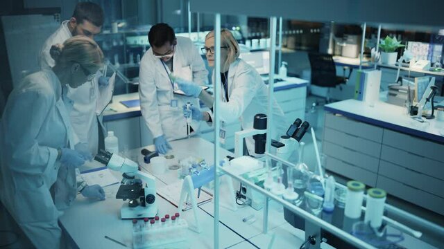 Team of Medical Research Scientists Have Meeting and Conduct Experiments with Help of DNA Samples in Test Tubes and Microscope Slides. Applied Science Laboratory with Diverse Multicultural Colleagues.