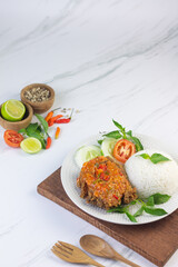 Ayam geprek, Indonesian popular streed food, made from crispy chicken smashed with sambal or chili sauce, eat with rice and cucumber, lettuce, tomato and kemangi. Isolated background, copy space.