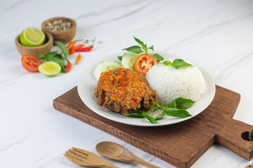Ayam geprek, Indonesian popular streed food, made from crispy chicken smashed with sambal or chili sauce, eat with rice and cucumber, lettuce, tomato and kemangi. Isolated background, copy space.